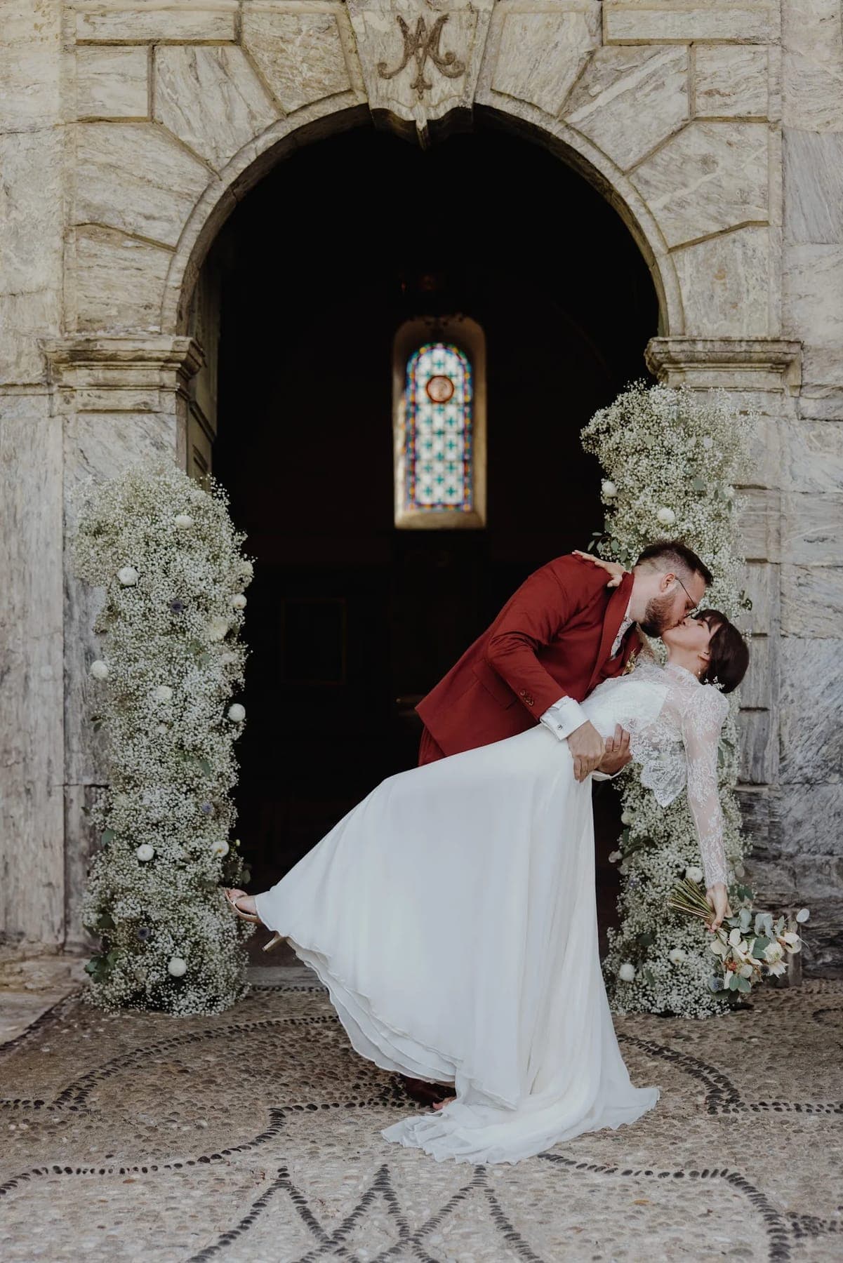 Mariés sous une arche de fleurs séchées, devant une porte en pierre