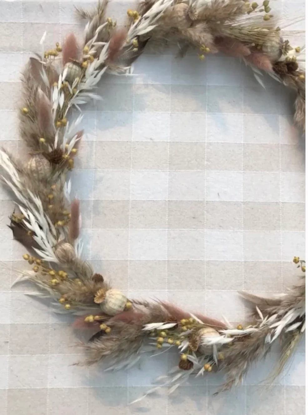 Couronne de fleurs et d'herbes séchées posée sur une nappe à carreaux